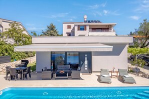 A modern two-story house with a swimming pool, outdoor seating, and a covered patio.