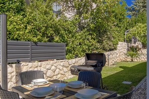 Un espacio exterior para comer con pared de piedra, una parrilla y una mesa lista para cuatro.
