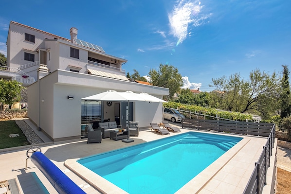 A modern house with a swimming pool, outdoor furniture, and a car parked nearby.