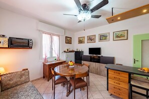 A compact living space with a dining table, chairs, a sofa, a kitchenette, a ceiling fan, and a TV. - Casa De Nardis Sunny House, Riva del Garda, Italy (Riva del Garda)