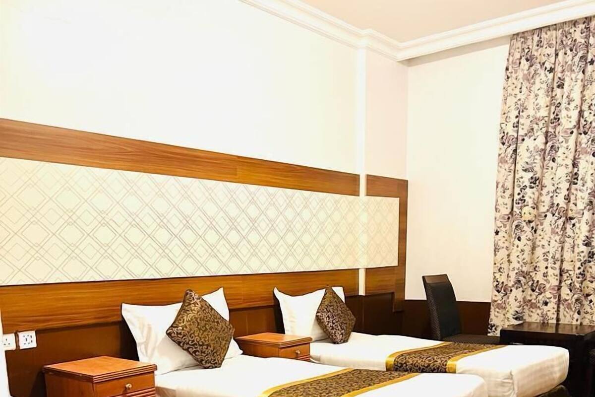 Une chambre d’hôtel avec deux lits simples, une tête de lit en bois, des rideaux à motifs et une moquette à motifs.