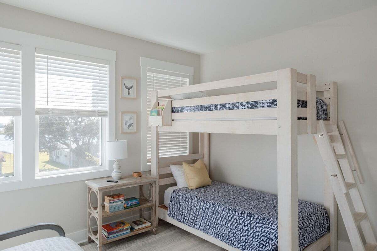 Habitación con literas, una escalera de madera, un escritorio con lámpara y una estantería.