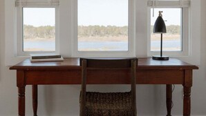Ett skrivbord i trä med en flätad stol, en lampa och en bok.
