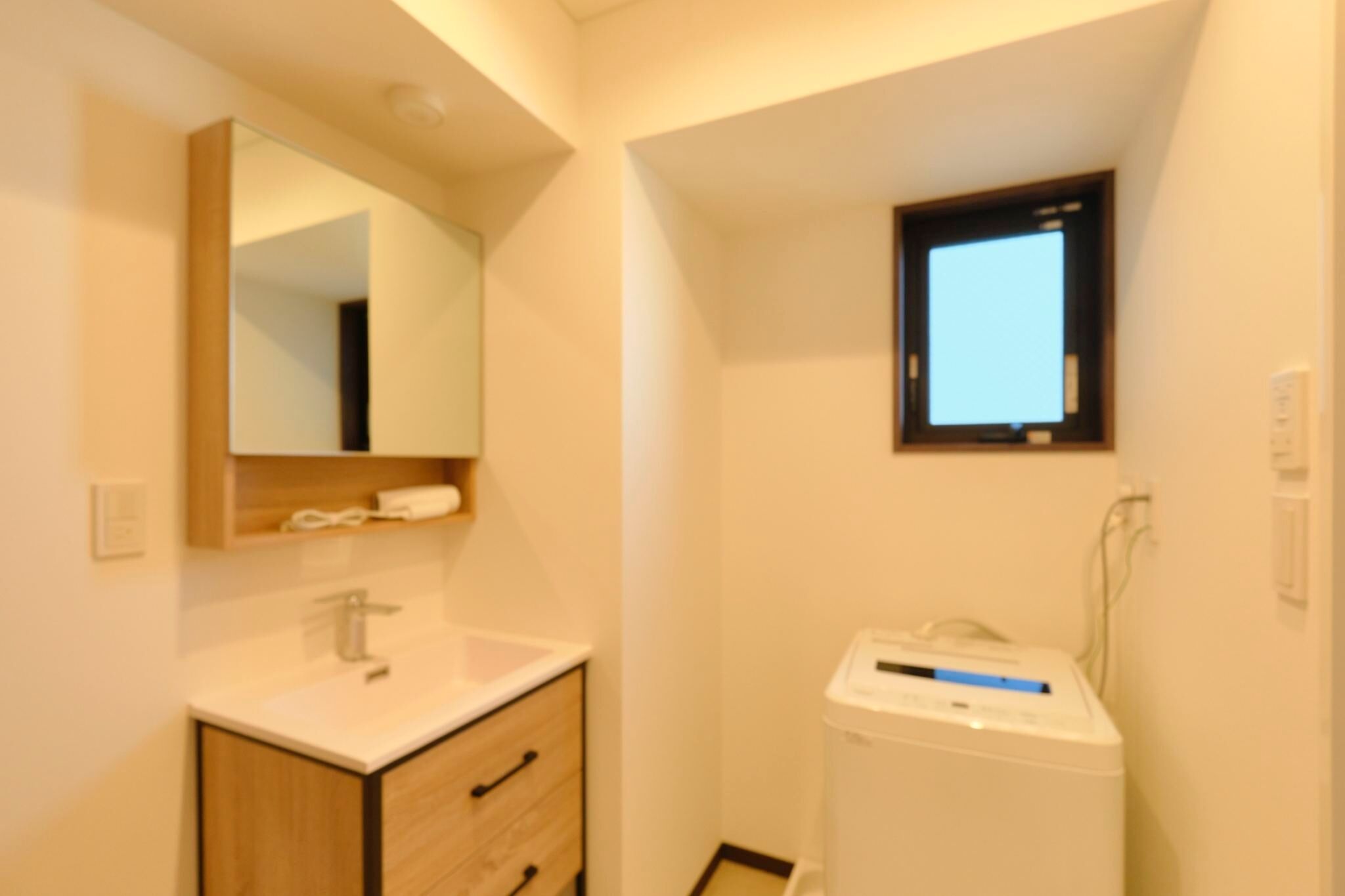 A bathroom with a sink, mirror, and a small window.