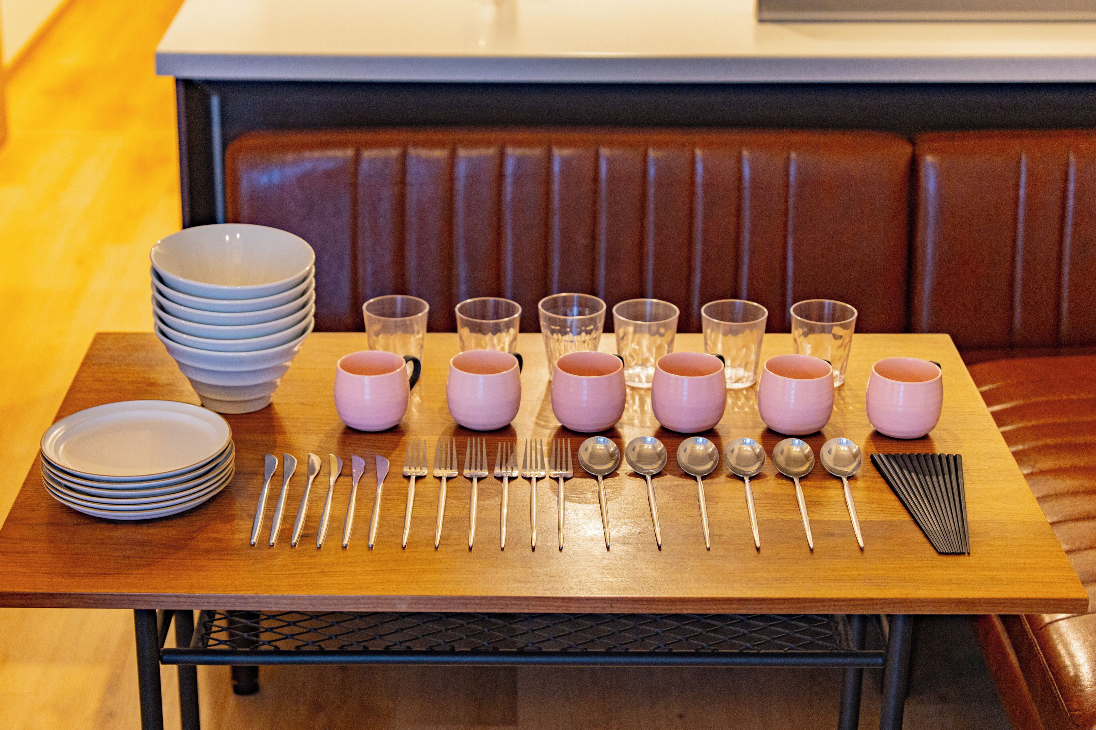A dining table set with plates, cutlery, and pink cups.