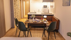 A compact hotel room with a dining table, two chairs, a sofa, a TV, and a kitchenette. - MODELLO Sangenjaya by Tranova (Tokyo)