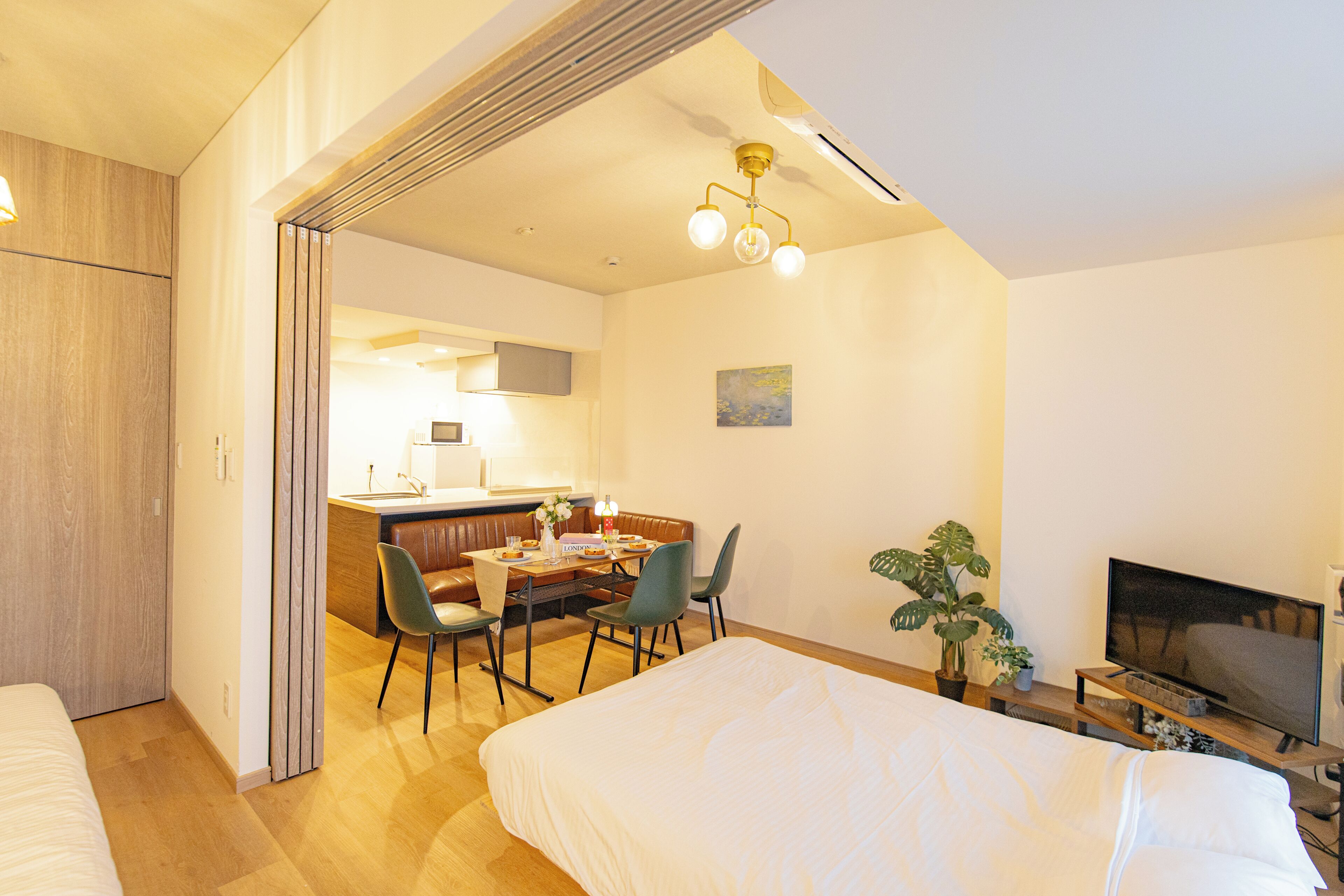 Quarto de hotel com cama, secretária e cadeiras, televisão e planta em vaso.