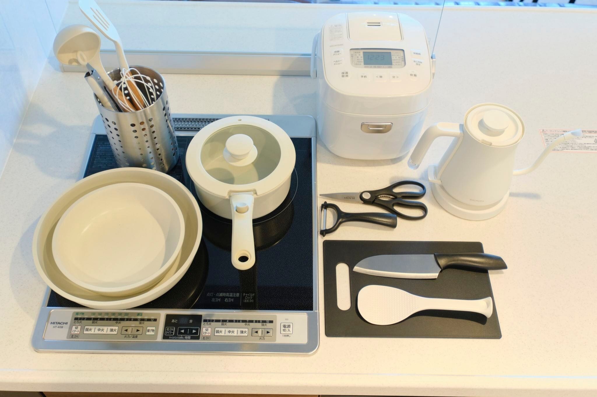A kitchen counter with a rice cooker, a coffee maker, a kettle, a set of kitchen utensils, and a digital scale.
