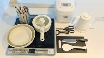 A kitchen counter with a rice cooker, a coffee maker, a kettle, a set of kitchen utensils, and a digital scale.