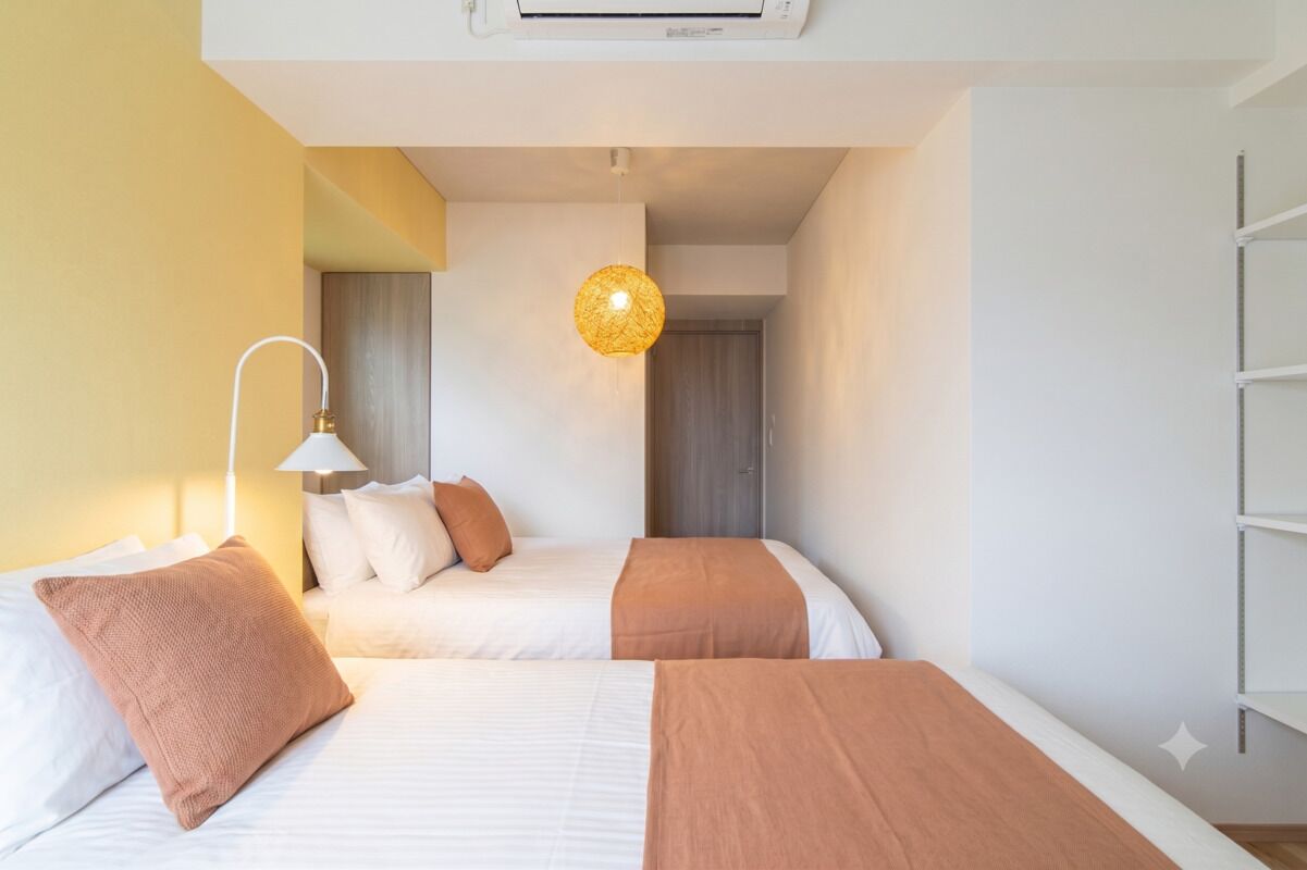 Ein Hotelzimmer mit zwei Betten, einer Nachttischlampe, einer Pendelleuchte und einer weißen Klimaanlage.