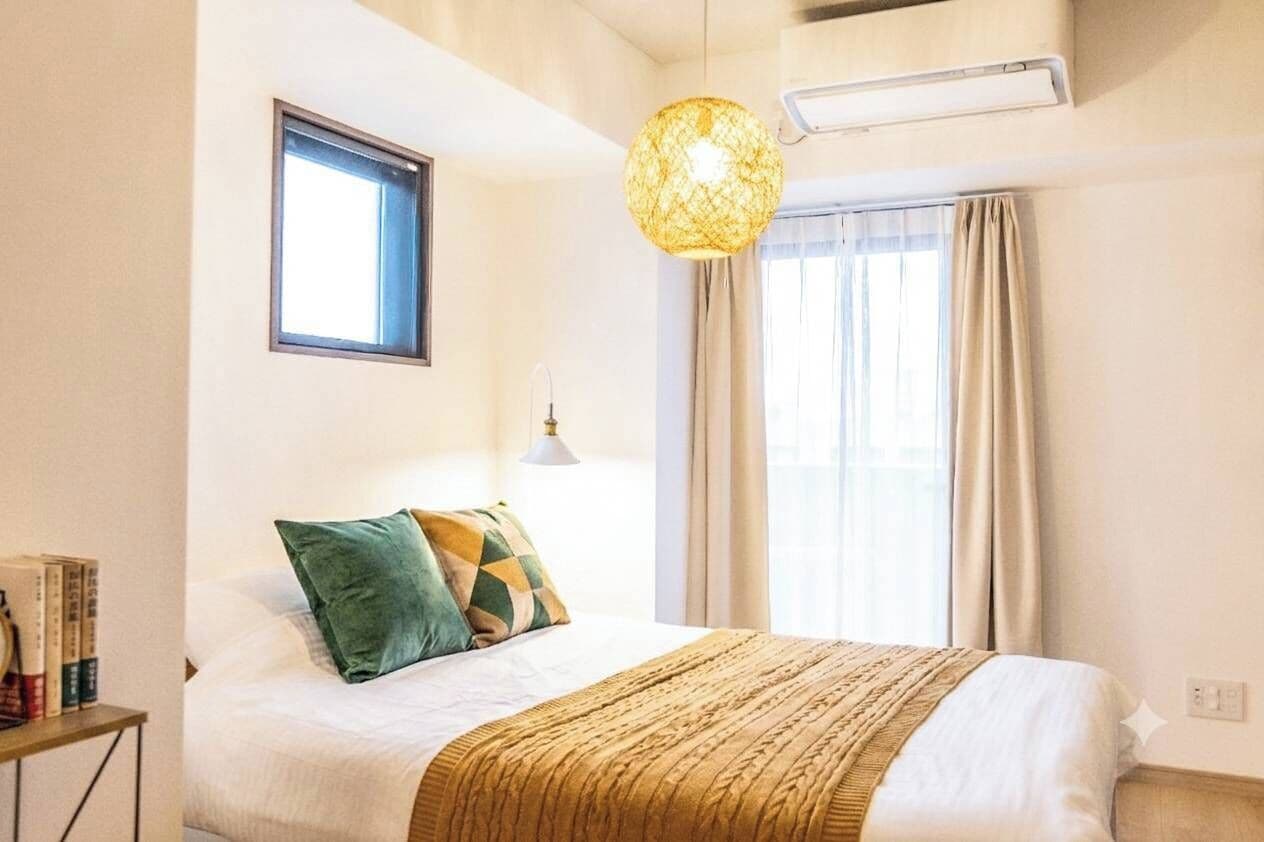 Ein Hotelzimmer mit Bett, Fenster, Pendelleuchte und Nachttisch mit Büchern.