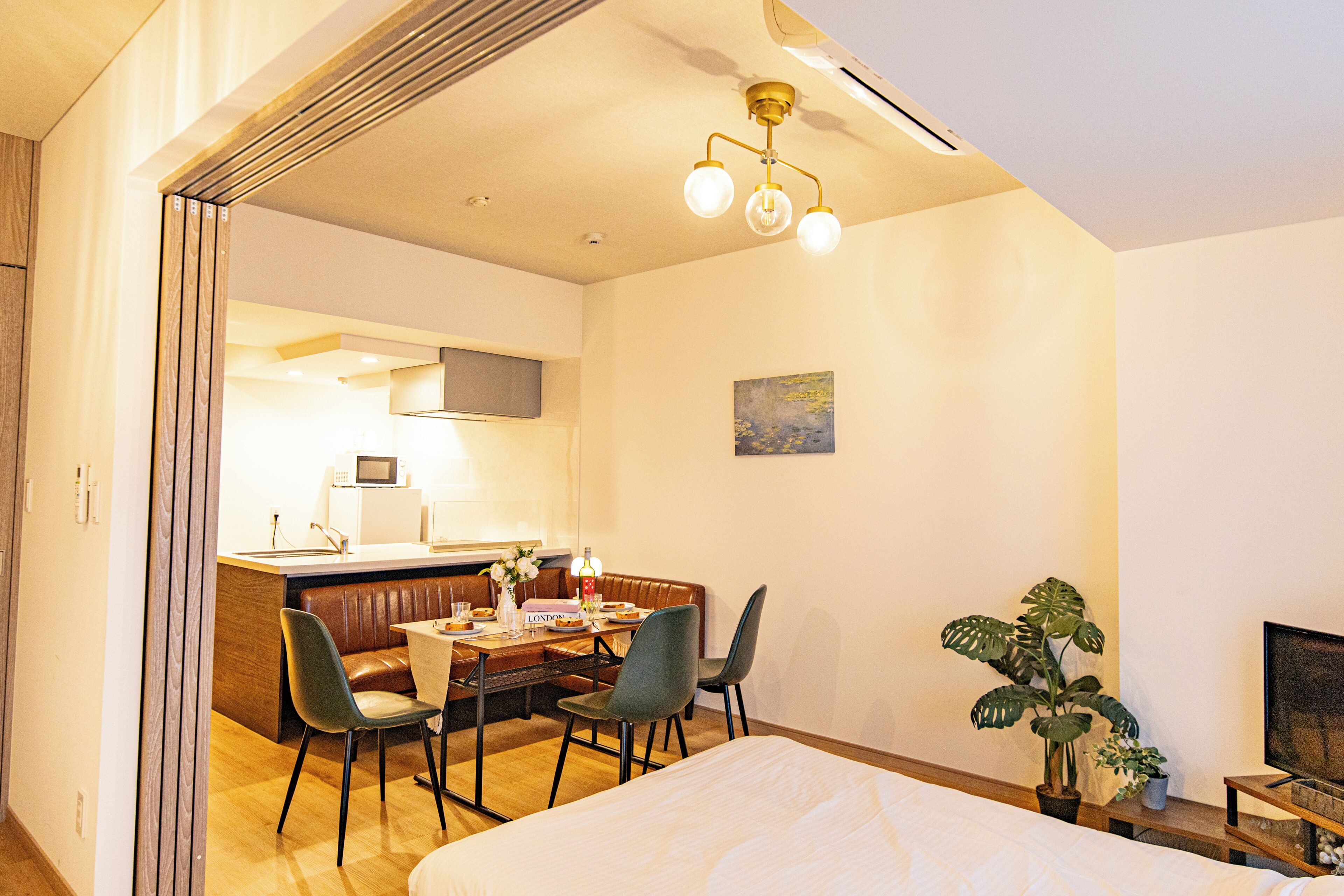 A hotel room with a bed, a dining table with chairs, a kitchen area, and a television.