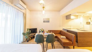 A modern hotel room with a bed, a sofa, a dining table with chairs, a TV, and a kitchenette. - MODELLO Sangenjaya by Tranova (Tokyo)