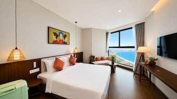 Habitación de hotel con una cama grande, un sofá, un televisor y vista al mar.