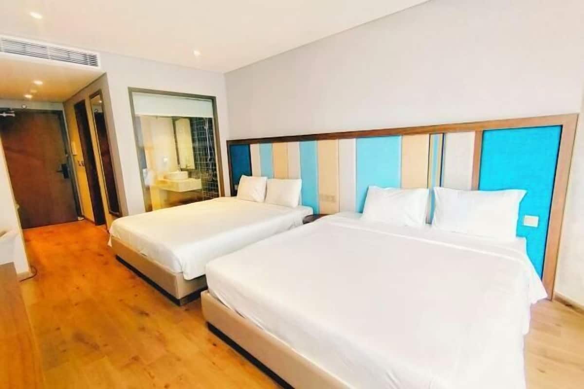 A hotel room with two beds, a wooden floor, a large mirror, and a blue accent wall.