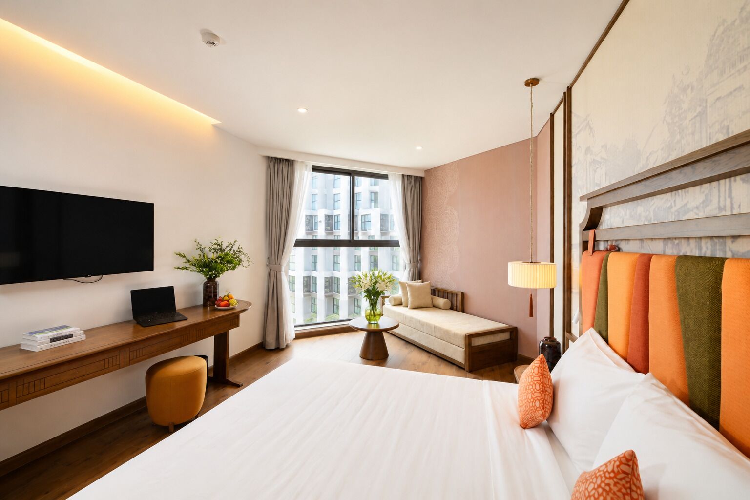 Quarto de hotel com uma cama, uma escrivaninha com um laptop, uma televisão e uma janela com cortinas.
