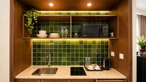 Cocina compacta con lavamanos, microondas y encimera con hervidor y botellas de agua.