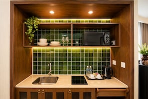 A compact kitchen with a sink, a microwave, and a countertop with a kettle and water bottles. - Apec Mandala Mui Ne by Dolphin Hospitality (Mui Ne)
