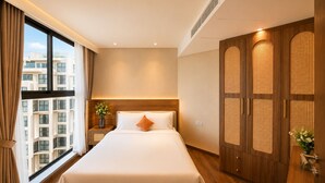 Habitación de hotel con una cama grande, un armario con diseño tejido, una mesita de noche con un florero y vistas a un edificio a través de la ventana.