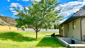 A house with a well-maintained lawn, a tree, and a patio area.
