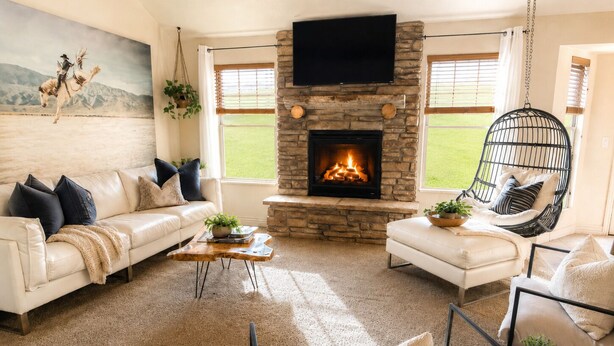 A living room with a stone fireplace, a white sofa, a hanging chair, and a painting on the wall.