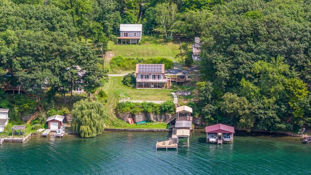 Vue aérienne d’une propriété au bord du lac, comprenant une maison principale, un quai et un petit bateau.