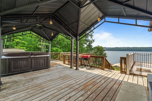 A covered deck with a hot tub, barbecue grill, and a view of a lake.