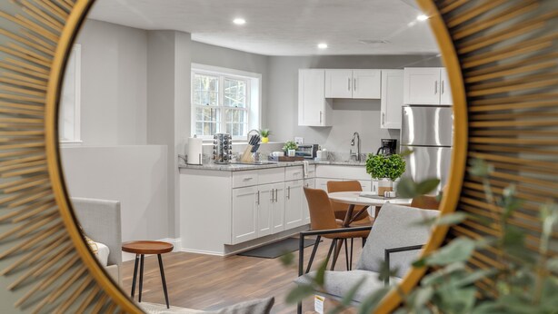 A modern kitchen with white cabinets, a stainless steel refrigerator, and a dining area with a table and chairs. - Cozy Chic Countryside Haven -  Sleeps 4 , Firepit (Sturbridge)