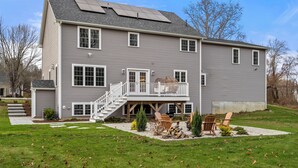 A two-story house with a covered deck, a staircase leading to a second-floor balcony, and a small outdoor seating area with chairs and a fire pit. - Cozy Chic Countryside Haven -  Sleeps 4 , Firepit (Sturbridge)