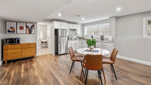 A modern kitchen with white cabinets, a stainless steel refrigerator, and a dining area with a round table and four chairs. - Cozy Chic Countryside Haven -  Sleeps 4 , Firepit (Sturbridge)