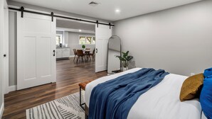 A bedroom with a bed, a sliding door leading to a dining area, and a plant. - Cozy Chic Countryside Haven -  Sleeps 4 , Firepit (Sturbridge)
