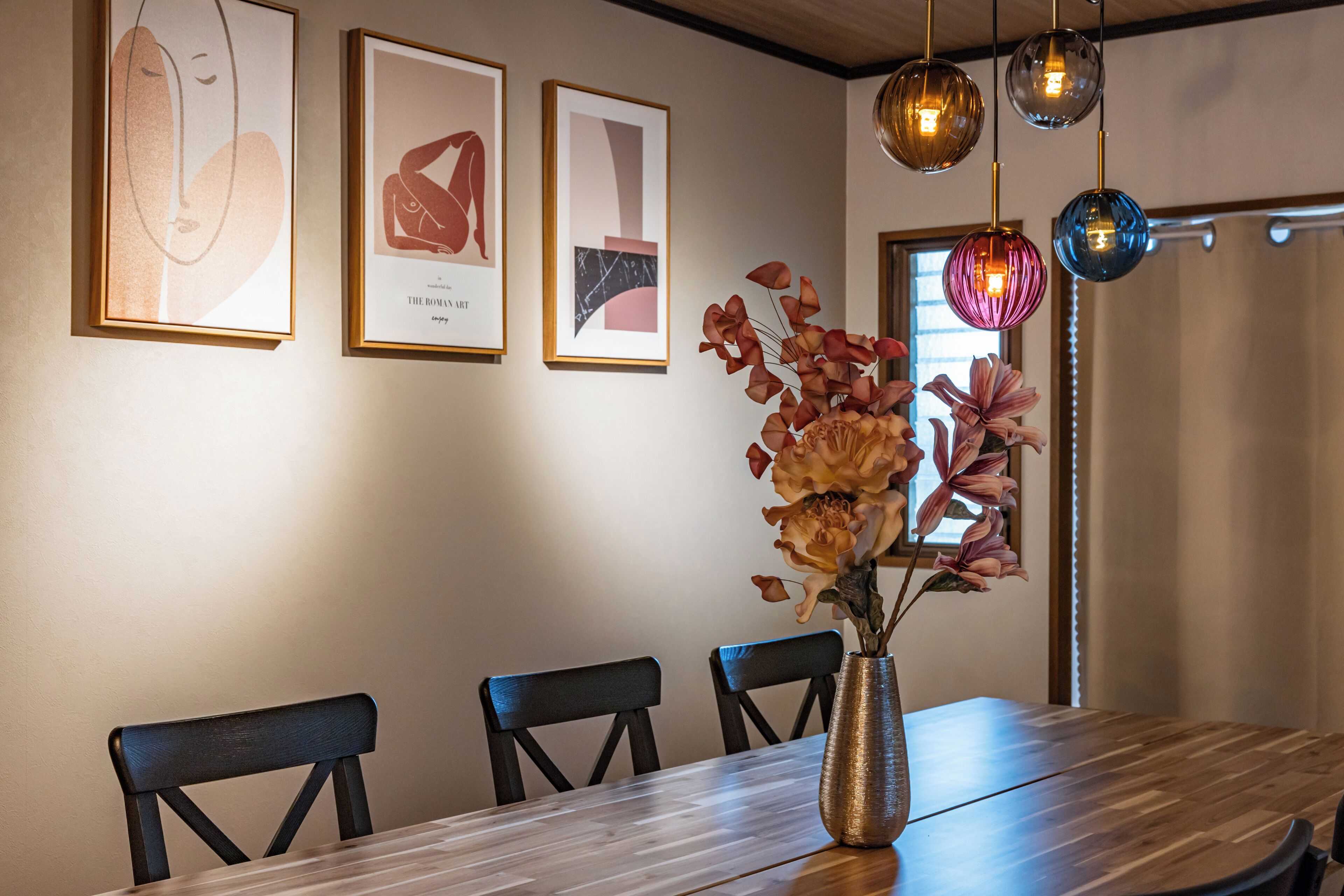 A dining area with a wooden table, chairs, a vase with flowers, and framed artwork on the wall.