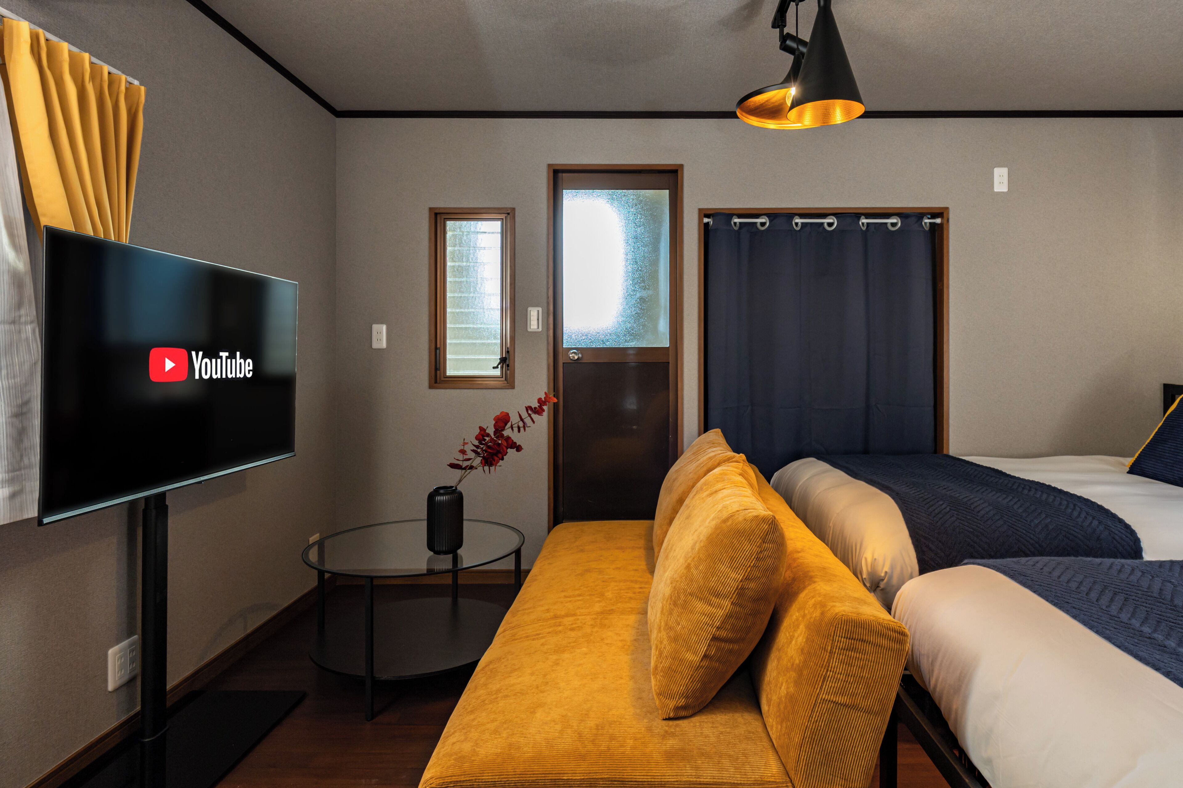 Habitación de hotel con sofá, dos camas, televisión, una mesita y una ventana con cortinas.