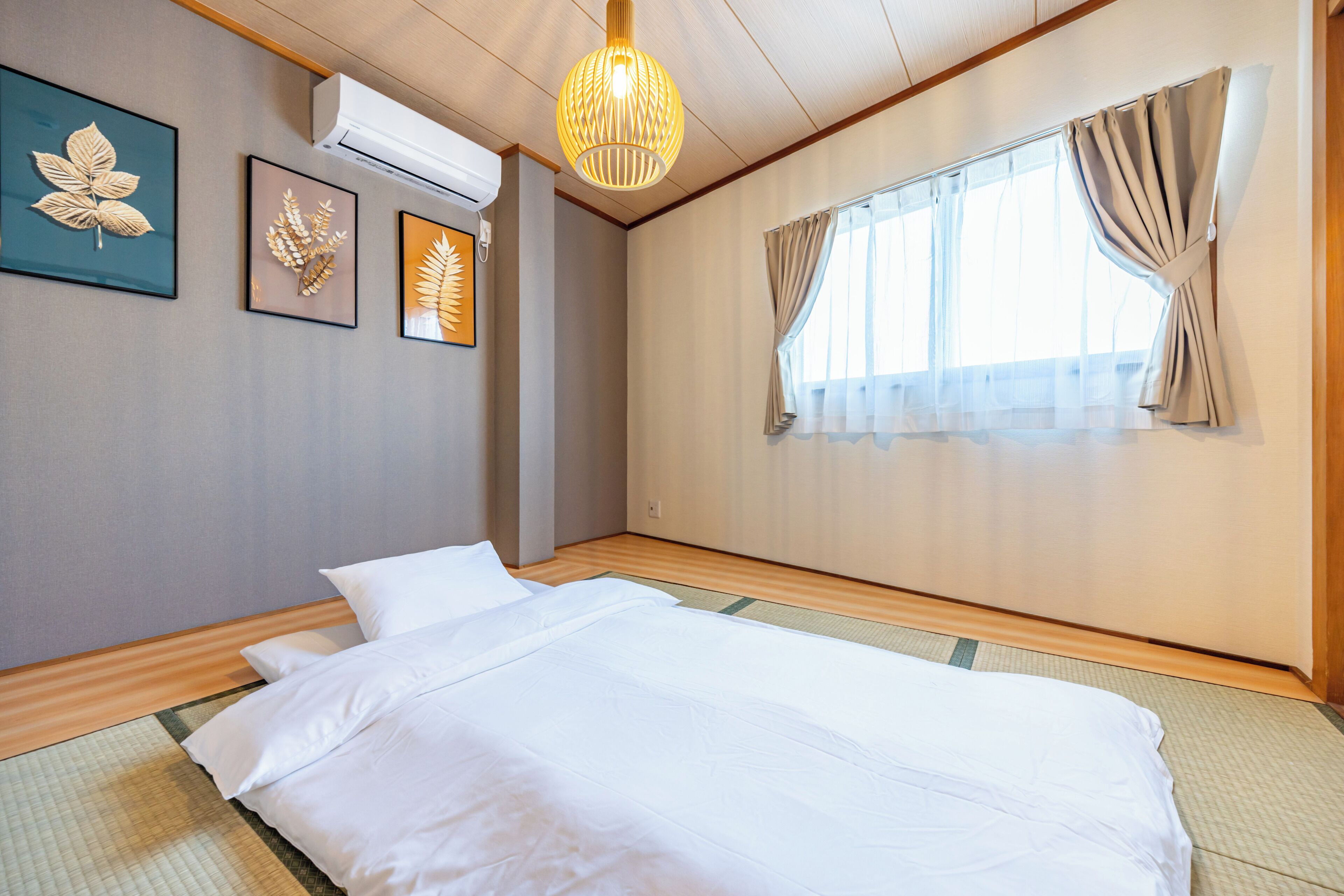 Una cama bien hecha en una habitación con un ventanal grande, equipo de aire acondicionado y decoración mural.