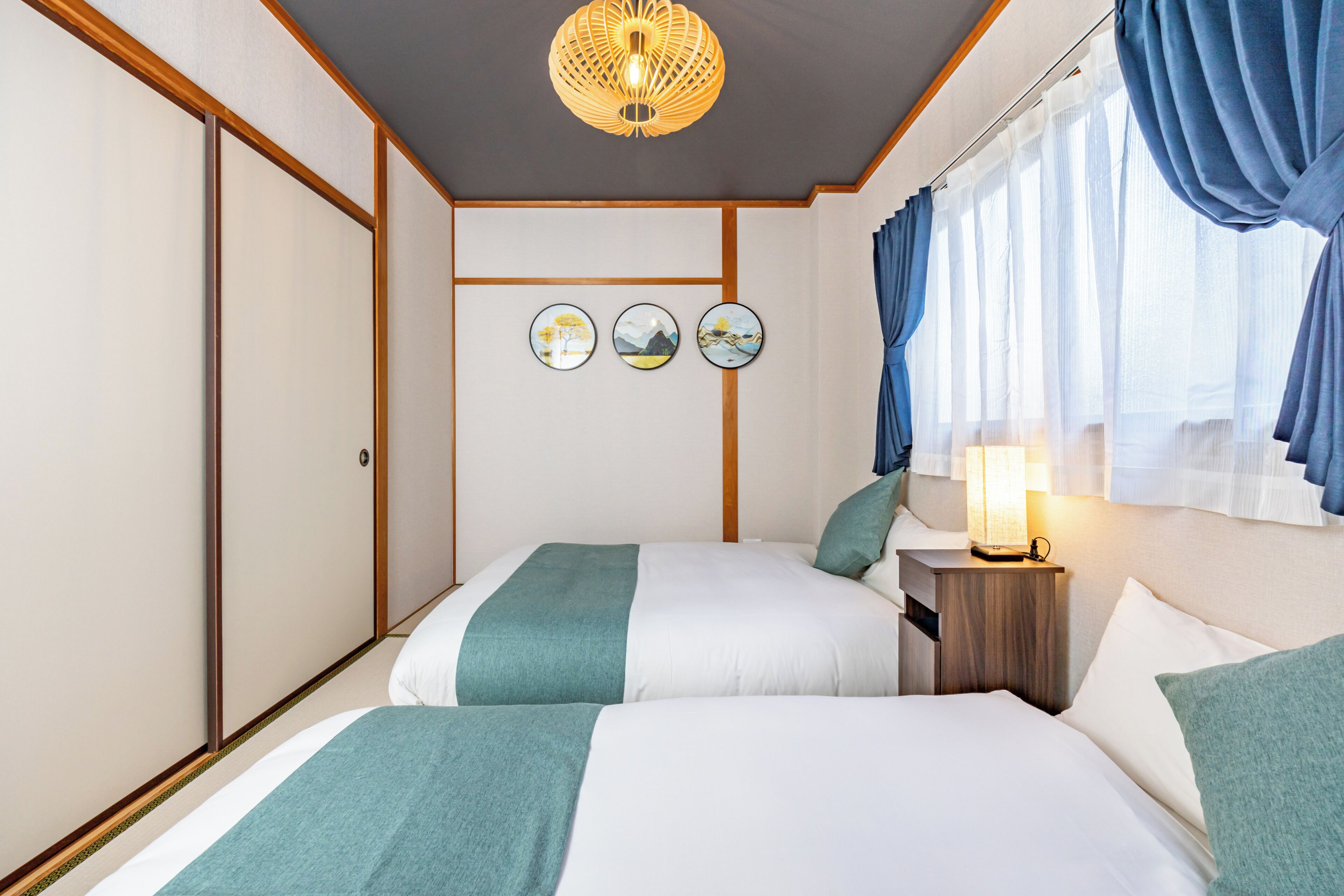 A hotel room with two beds, a nightstand, a lamp, and three wall-mounted pictures.