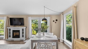 A modern living room with a fireplace, a dining table with chairs, a TV mounted above the fireplace, and large windows with curtains. - Beautiful 3-bed home with Canandaigua Lake view and access, Bristol Ski, Winery (Canandaigua)