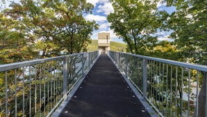 A pedestrian bridge with metal railings and a black surface, surrounded by trees and a body of water. - Beautiful 3-bed home with Canandaigua Lake view and access, Bristol Ski, Winery (Canandaigua)