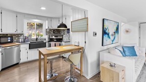 A modern kitchen with white cabinets, a wooden dining table, and bar stools. There is a white sofa with blue pillows in the adjacent living area. - Beautiful 3-bed home with Canandaigua Lake view and access, Bristol Ski, Winery (Canandaigua)