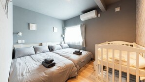A bedroom with two beds, a crib, a window with curtains, and an air conditioning unit. - THE COMFY SAPPORO (Sapporo)