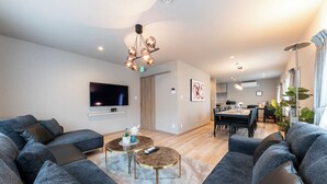 A modern living room with a flat-screen TV, grey sofas, round coffee tables, and a dining area with a table and chairs. - THE COMFY SAPPORO (Sapporo)