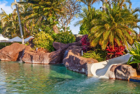 A pool with a water slide, large rocks, and tropical vegetation.