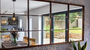 Un comedor con un espejo grande que refleja una cocina y una vista de un jardín a través de un ventanal.