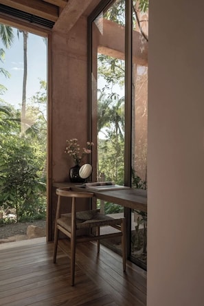 Ein Zimmer mit einem Holztisch, einem Stuhl und einem Fenster mit Blick auf Grünflächen.
