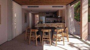 A modern kitchen with wooden cabinets, a central island, and a dining area with wooden chairs. - Rosa Morada: Luxury Villas with Private Beach (San Francisco)