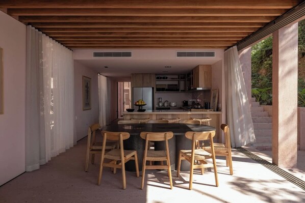 A modern kitchen with wooden cabinets, a central island, and a dining area with wooden chairs.