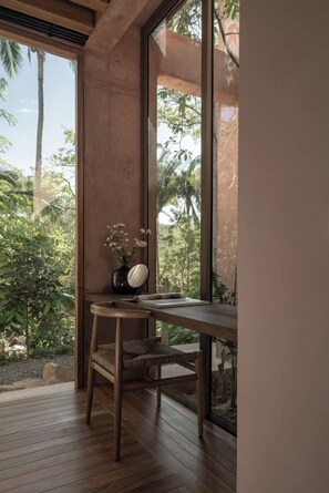 A room with a wooden desk, a chair, and a window overlooking greenery.