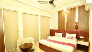 A modern hotel room with a large bed, a small sofa, a bedside table, and a ceiling fan. - Om B & B (Amritsar)
