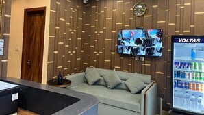 A reception area with a wooden panel wall, a mounted TV, a couch, and a VOLTAS refrigerator. - Om B & B (Amritsar)