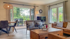 A spacious living room with a wooden coffee table, comfortable seating, a TV, and large windows offering a view of greenery. - Lovely home in Paasloo with WiFi (Paasloo)