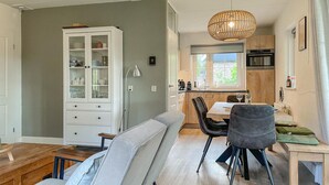 A modern kitchen with a dining area, featuring a cabinet with glass doors, a dining table with chairs, and a hanging light fixture. - Lovely home in Paasloo with WiFi (Paasloo)